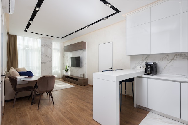 apartment kitchen and living room with white cabinets and counters and hardwood floors